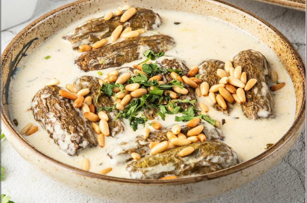Bowl of Shakh Almahshi with rice and pine nuts on a stone surface, featuring Tazweed Catering Services branding.